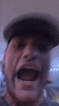 a man in a hat is making a funny face with his mouth open .