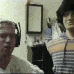 a man wearing headphones and a striped shirt stands next to another man