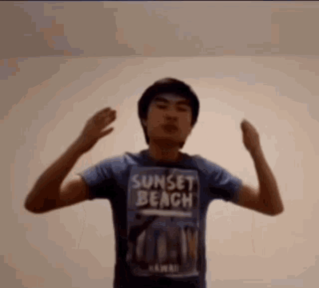 a young man wearing a blue sunset beach t-shirt is flexing his muscles .