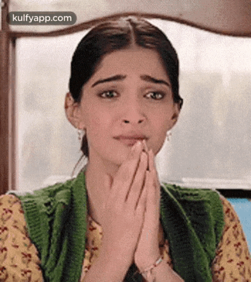 a woman in a green sweater is praying with her hands folded in front of her face .