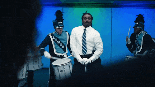 a man in a white shirt and tie is playing a drum