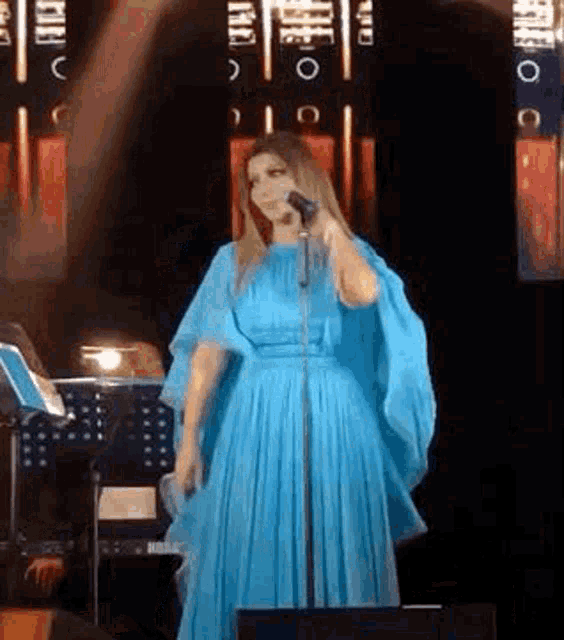 a woman in a blue dress is singing into a microphone while standing on a stage .