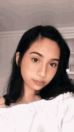 a young woman with dark hair is wearing a white shirt