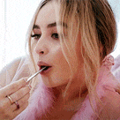 a woman in a pink dress is eating something with a spoon in her mouth .