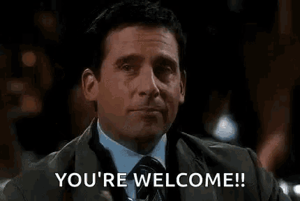 a man in a suit and tie is holding a drink in his hand and saying `` you 're welcome '' .