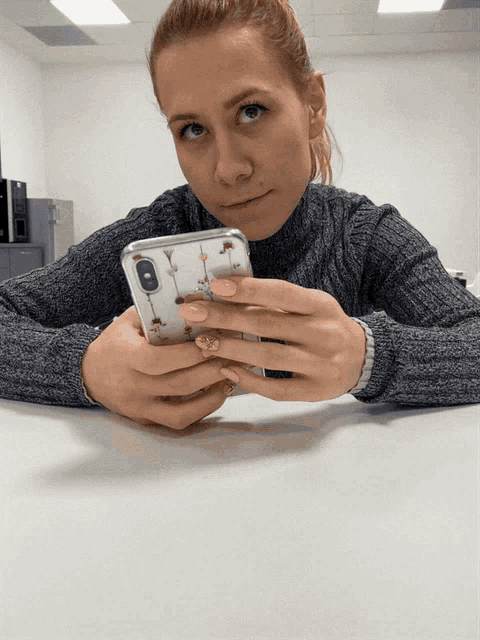 a woman sitting at a table holding a cell phone with a giraffe case on it