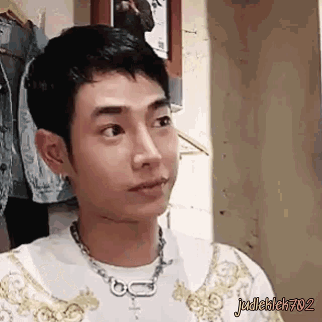 a young man wearing a necklace and a white shirt is standing in a room .