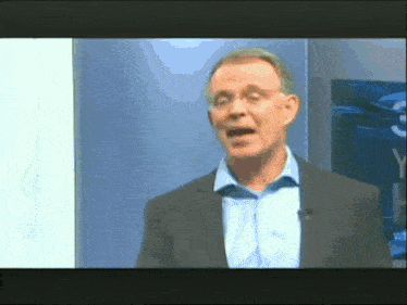 a man in a suit and blue shirt is standing in front of a wall with the letter y on it
