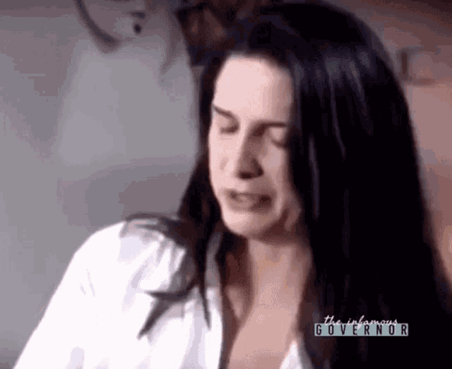 a woman with long black hair is crying while wearing a white shirt with the words the infamous governor written on it .