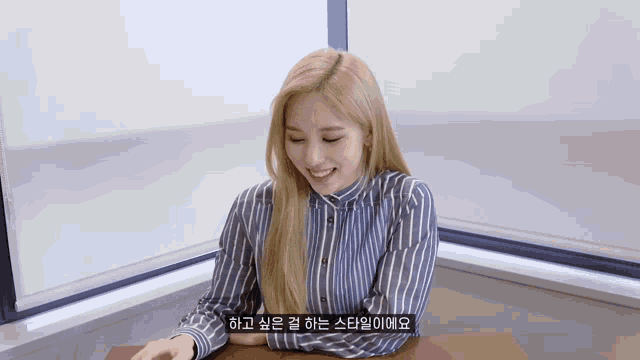 a woman in a striped shirt is smiling and sitting at a desk