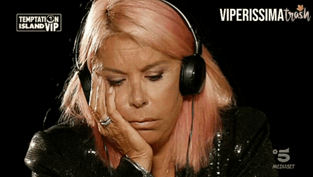 a woman with pink hair is wearing headphones and watching temptation island vip on tv