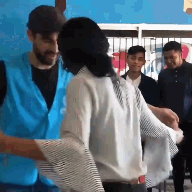 a man in a blue vest is hugging a woman in a white striped shirt