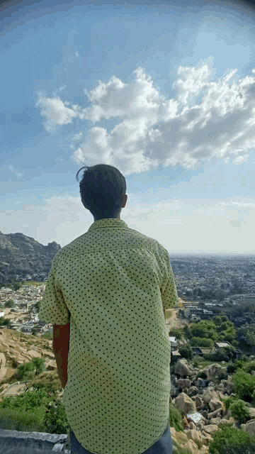 a man in a polka dot shirt is standing on a hill overlooking a city