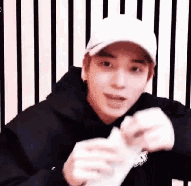 a young man wearing a white hat and a black hoodie is holding a piece of paper .