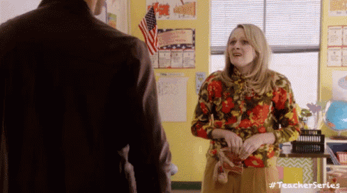 a woman in a floral shirt is standing in a classroom with a man .
