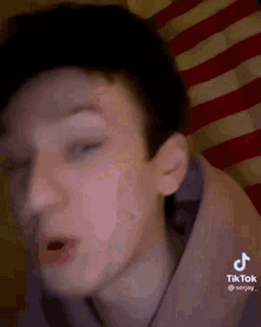 a young man is making a funny face in front of a red and white american flag .
