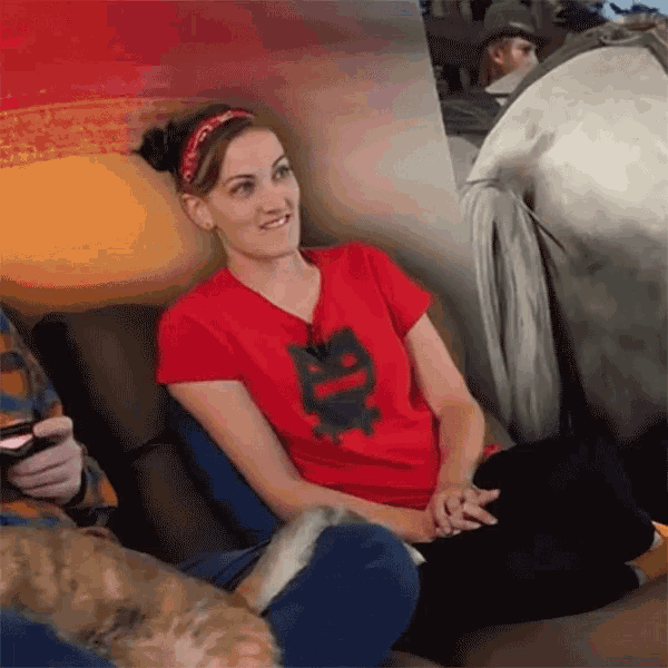a woman wearing a red shirt with a black cat on it sits on a couch