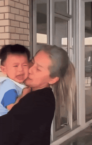 a woman is holding a baby who is crying and kissing it on the cheek