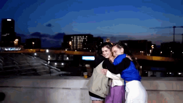two women hugging each other in front of a city at night