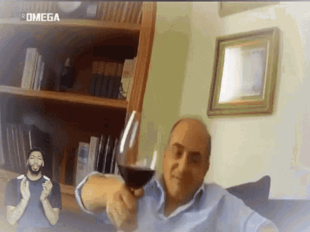 a man is holding a glass of wine in front of a bookshelf with the word omega on it