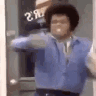 a man in a blue shirt and tie is standing in front of a door with his arms outstretched .
