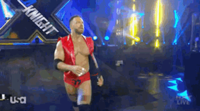 a wrestler in a red outfit is walking through a tunnel with the word knight on it