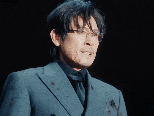 a man wearing glasses and a suit is smiling with blood on his face