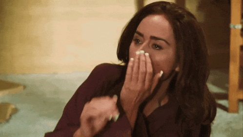 a woman covering her mouth with her hands while sitting on the floor .