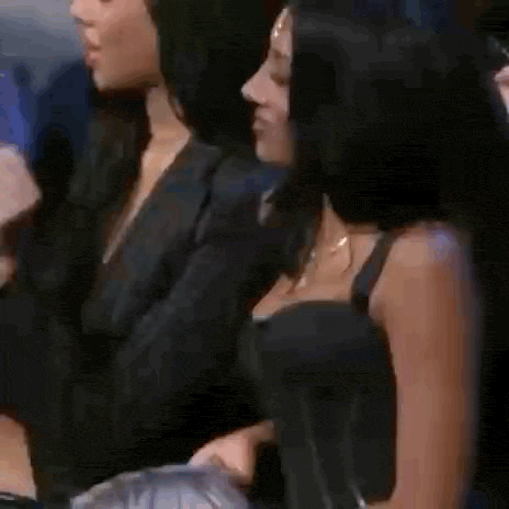 two women are sitting next to each other in a crowd . one of the women is wearing a black top .