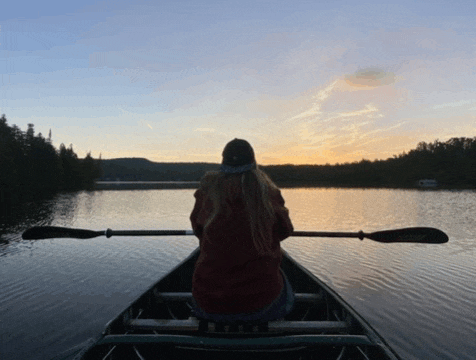a woman sits in a canoe with oars in the water at sunset