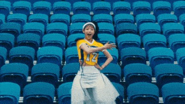 a woman in a yellow jersey with the number 12 on it stands in a stadium full of blue seats