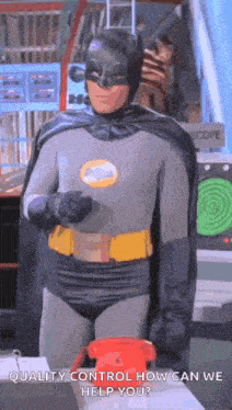 a man in a batman costume is standing next to a red telephone and talking on it .