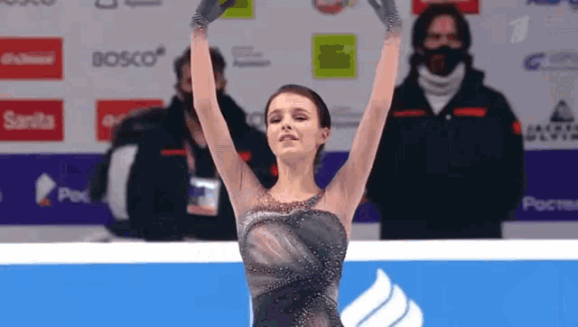 a woman in a black dress is holding her arms in the air while standing on a ice rink .