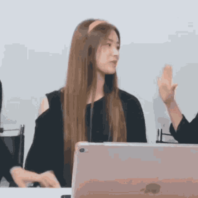 a woman is sitting at a table with a laptop and giving a high five .