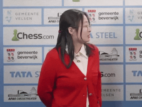 a woman in a red jacket is standing in front of a wall that says chess.com and tata steel