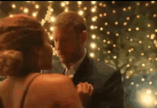 a man in a suit and a woman in a dress are dancing in front of christmas lights .