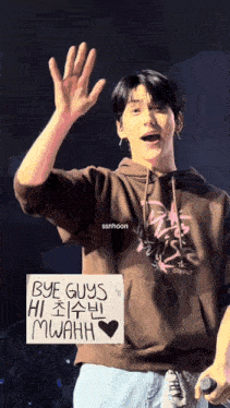 a man in a brown hoodie holds a sign that says bye guys hi mwahh