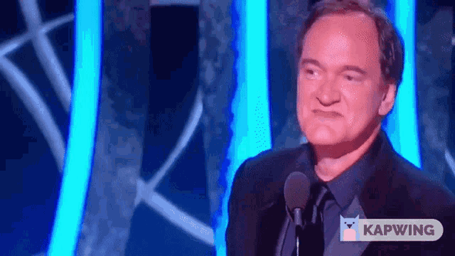 a man speaking into a microphone with a kapwing logo on the bottom right