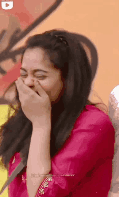 a woman in a pink shirt is laughing with her eyes closed