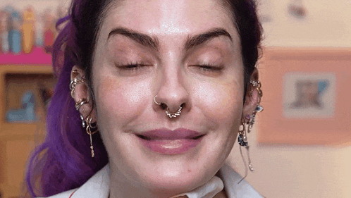 a woman with purple hair is smiling with her eyes closed