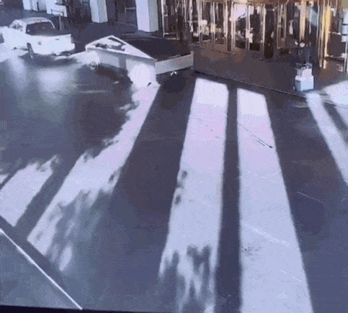 a white truck is driving down a street in front of a building with shadows on the ground