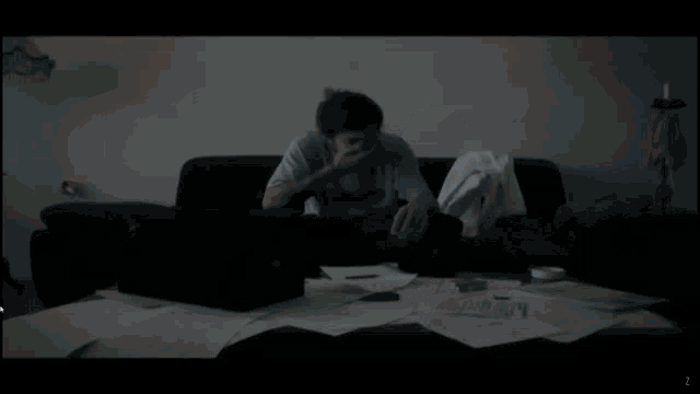 a man sits on a couch with his head in his hands and a stack of papers on the table
