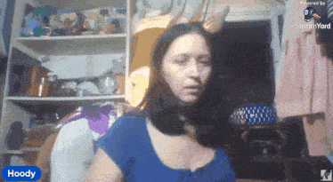 a woman in a blue shirt is sitting in front of a shelf and a sign that says hoody