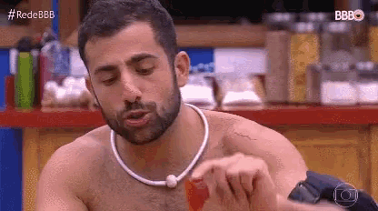 a shirtless man with a beard and a necklace is sitting at a table .