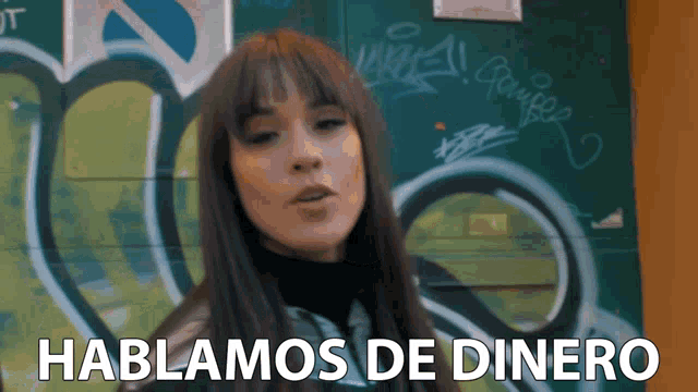 a woman stands in front of a wall with graffiti and the words hablamos de dinero