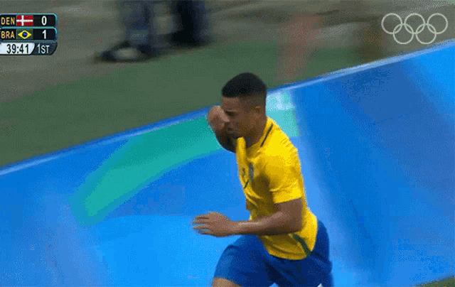a man in a yellow shirt and blue shorts is running in front of a scoreboard that says den 0 bra 1