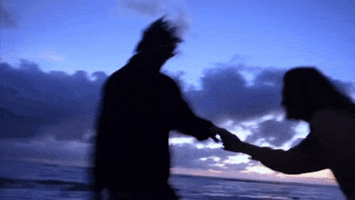 a man and a woman are holding hands on the beach at sunset