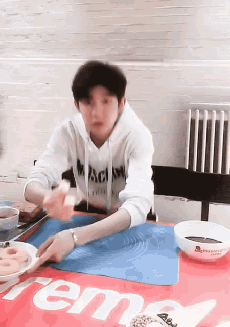 a man in a white hoodie sits at a table with a supreme logo on it