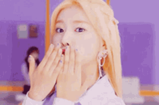 a woman with blonde hair and blue nails is blowing a kiss with her hands .