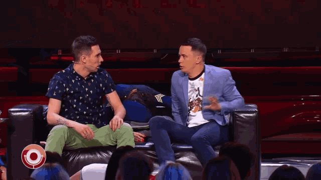 three men are sitting on a couch in front of a crowd with a target in the background